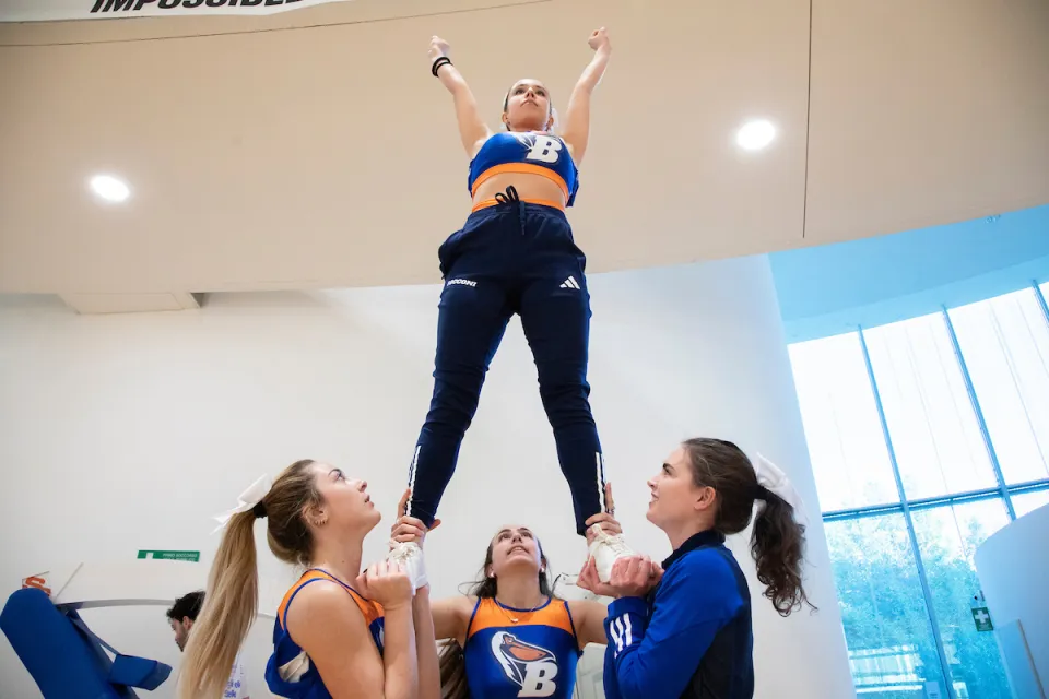 Three students on the cheerleading team raise up their teammate for acrobatic choreography.