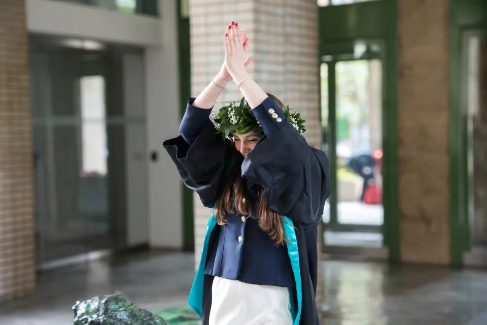 A newly graduated student gives a joyful applause between the lions at the entrance of the Sarfatti 25 building.