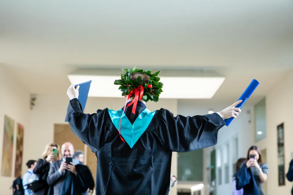 Uno studente posa con la tesi e la pergamena di laurea per le foto dei parenti.