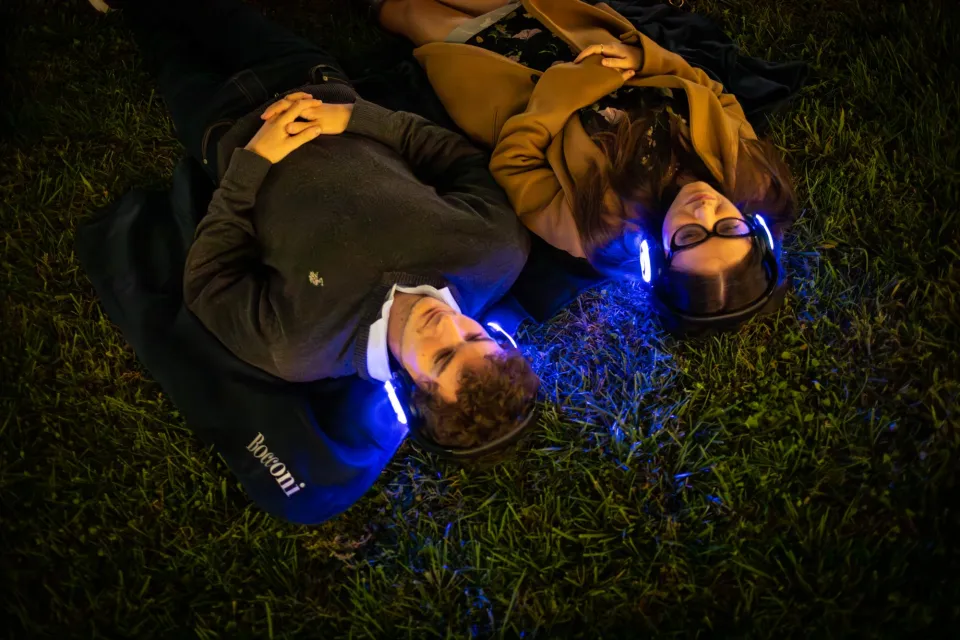 Una coppia di studenti stesa sul prato del nuovo campus Urbano si gode ad occhi chiusi l'ascolto del Silent Concert.