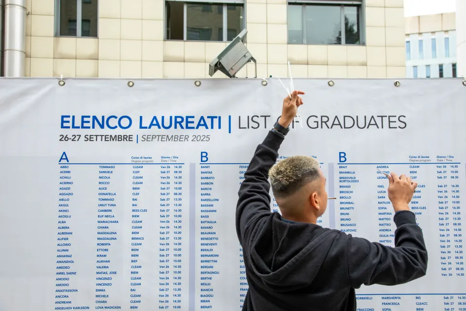 A student standing in front of the noticeboards listing graduates.