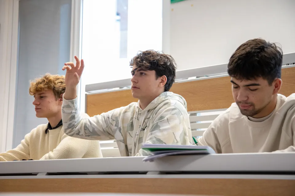 A student in a classroom raises his hand to ask for clarification.
