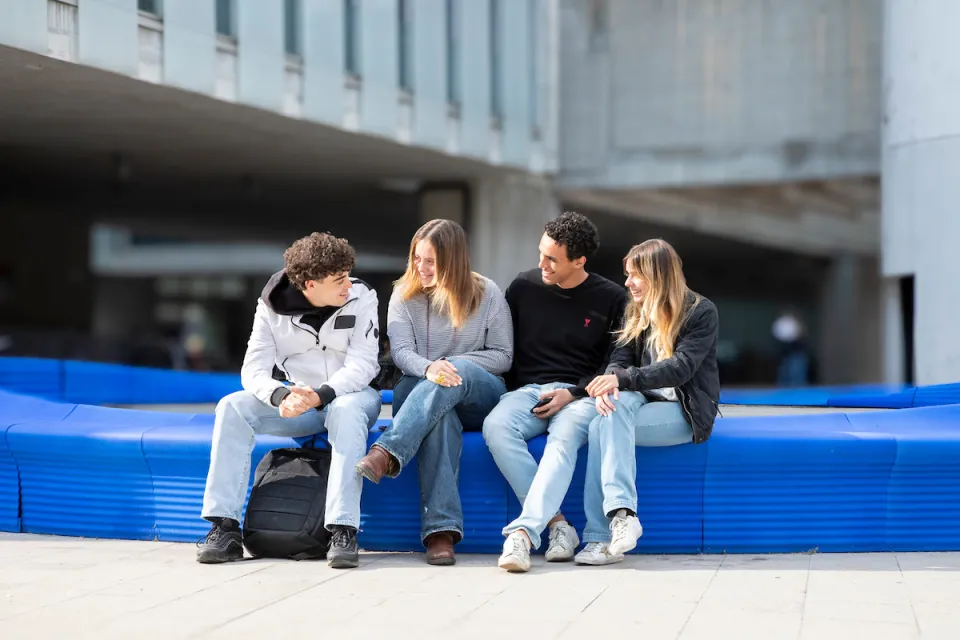 Students chat while sitting on the blue bench made from recycled materials.