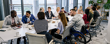 Gruppo di persone che incarnano alcune delle dimensioni della diversità (genere, provenienza, disabilità) in riunione attorno a un tavolo